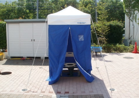 屋外に青いテントが設置され、正面のファスナーが開いて中の便座が見えている写真