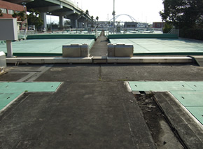 道路橋が通っている横の広い敷地に、緑の正方形型の蓋や装置が設置されている写真
