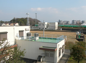 壁は白く、屋上部分は緑色の建物が、広い芝生の隣に建っている写真
