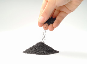 黒くて細かい粒状の活性炭を手から落とし、下に活性炭の小さな山が出来ている写真