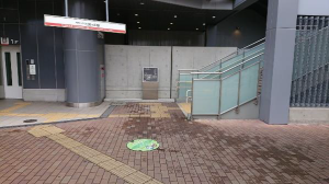 駅のエレベーターと階段の間のレンガ調のタイルの中にあるマンホールの写真