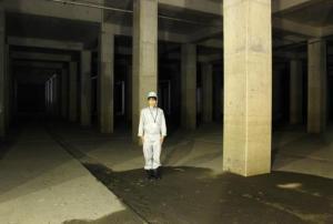 薄暗く大きな柱が何本も建っている調整池に関係者が一人立っている写真
