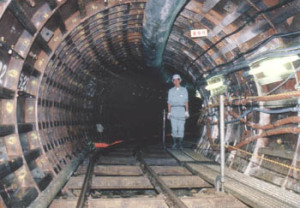 レールが通っている薄暗い下水管の内部をライトアップし、向かって右寄りに作業員の関係者が立っている写真