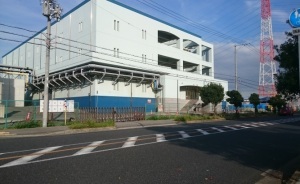 鉄塔の横に建っている白と青を基調とした大和川ポンプ場の外観写真
